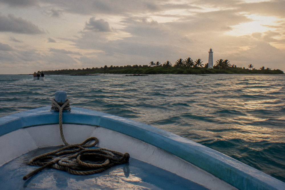 A tour boat riding a light swell on open water near a low island