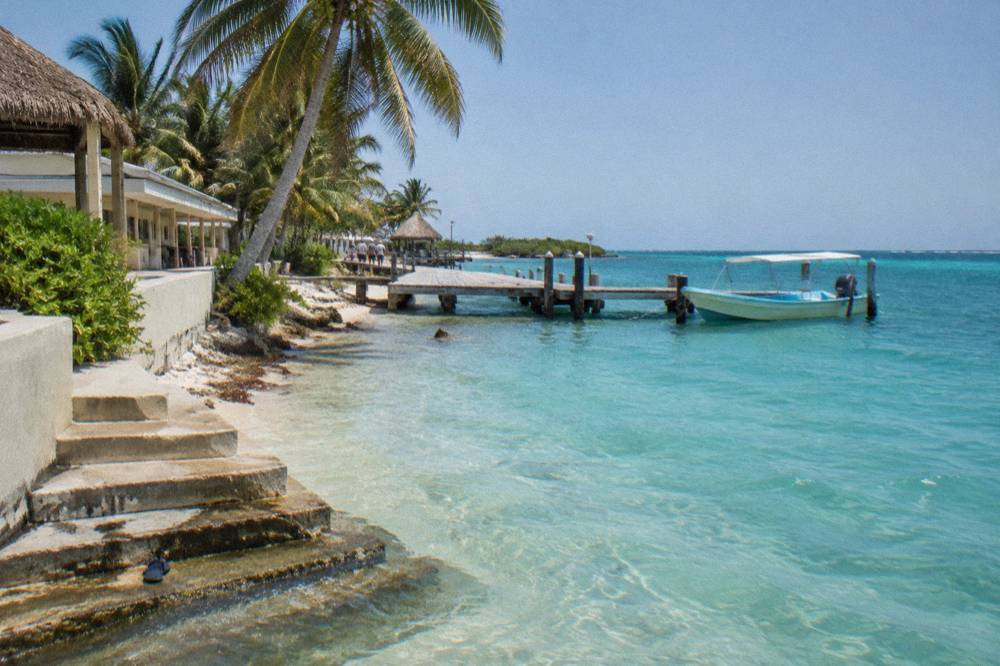 Beachfront resort-style building on a tropical shore with clear turquoise water and a small dock